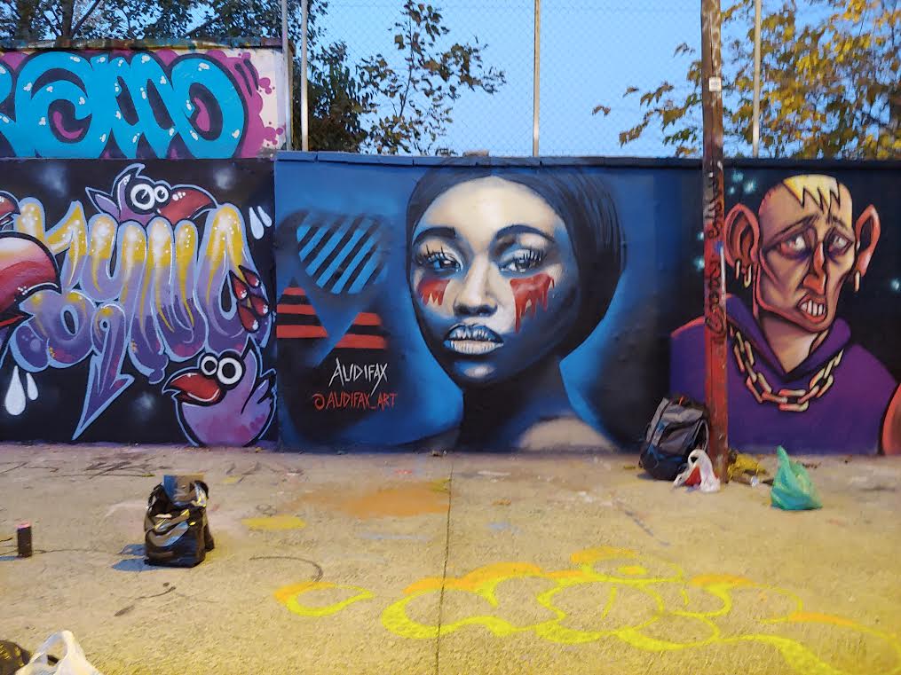 Image of spray paint mural showing person's face with red under their eyes and a dark blue background