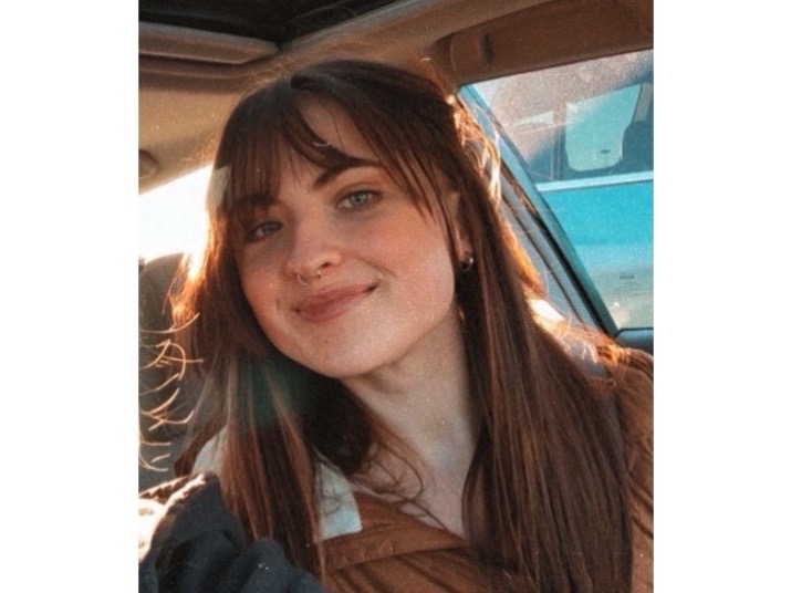 Image of photo of artist looking straight ahead and smiling with long brown/red hair