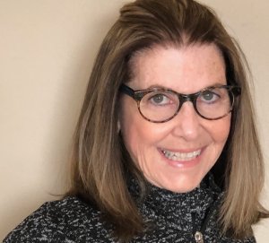 Image of photo of artist with shoulder-length brown hair and glasses smiling at the camera