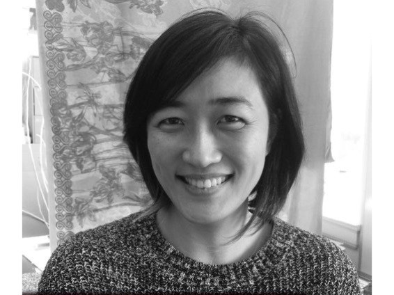 Image of black and white photo of artist with neck-length black hair, smiling at the camera.