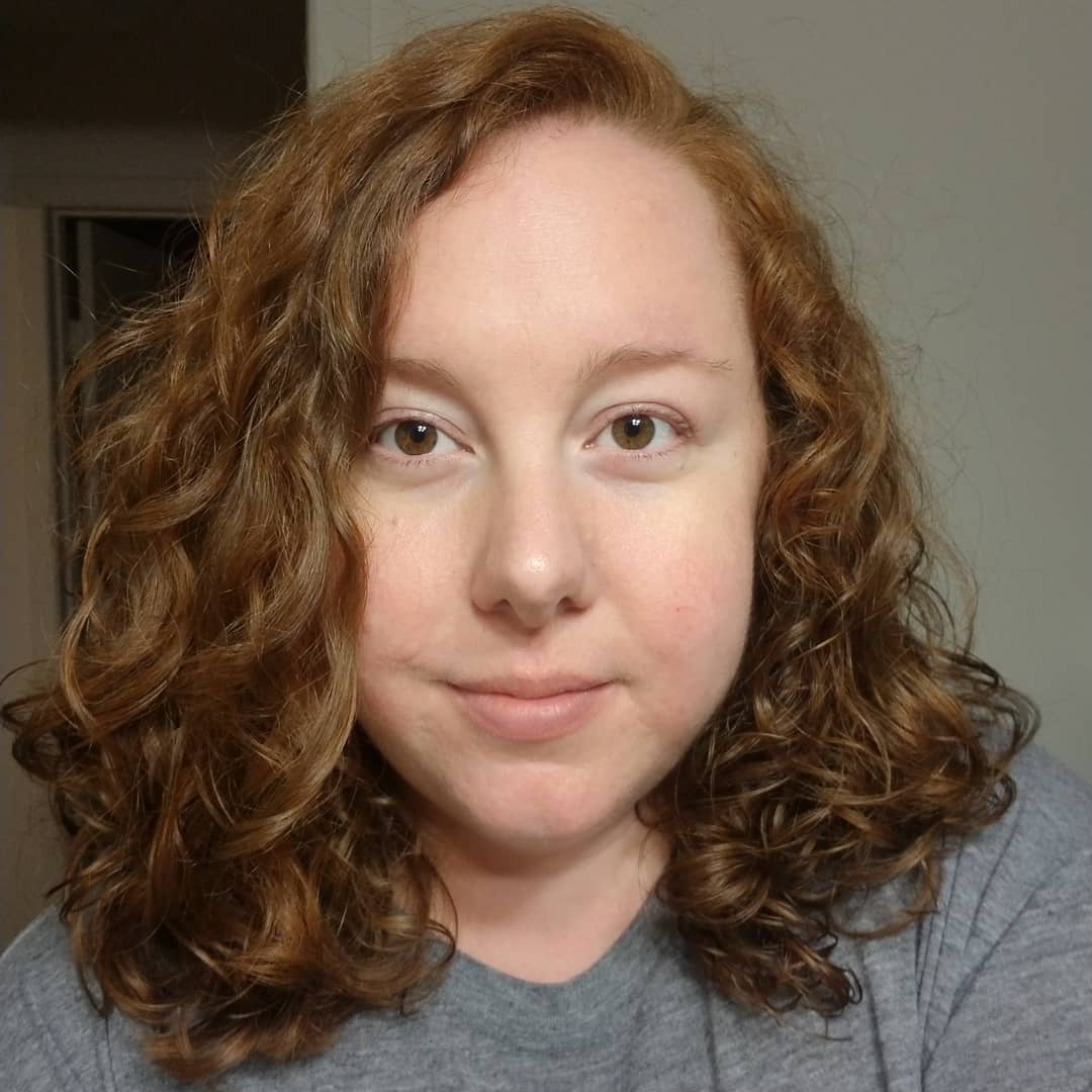 Image of Kelsey Foster. Kelsey is wearing a gray shirt and is pictured in front of a white wall.