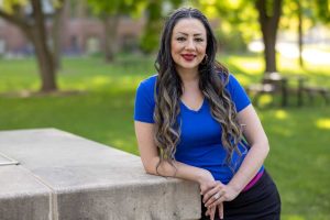 Picture of Sona Kazemi leaning on cement wall smiling in blue shirt
